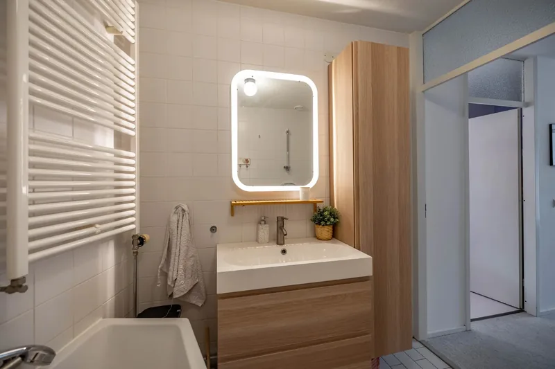 Voor: gedateerde badkamer met wit tegelwerk, ligbad en radiator